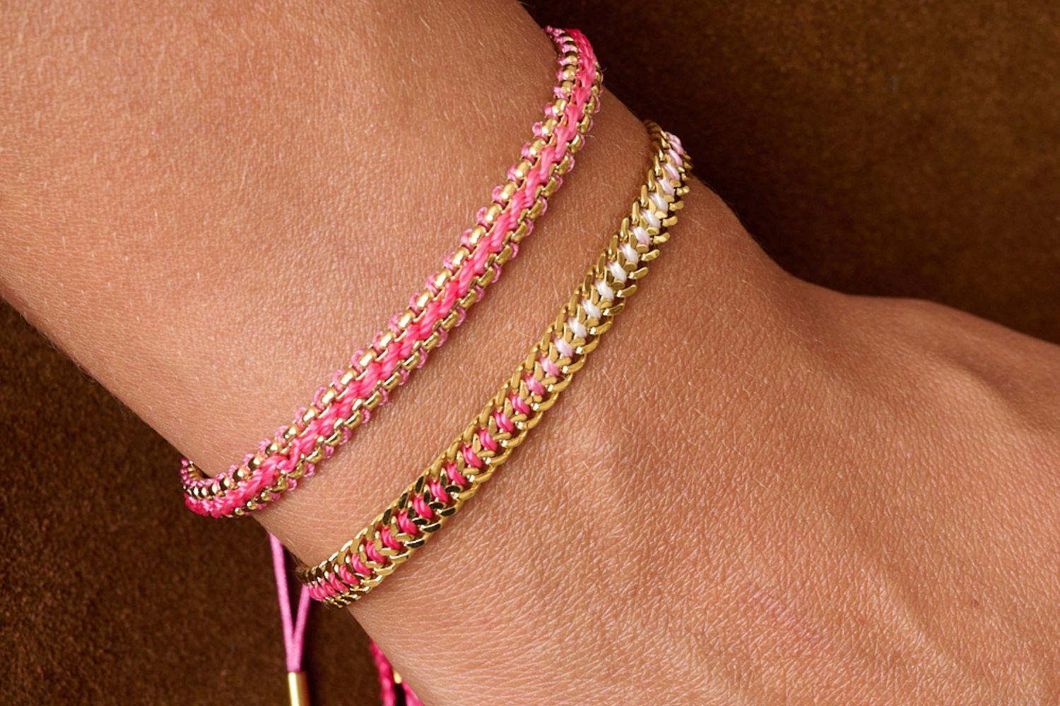 Two braided handwoven bracelets. Bloom Pink and Athena pink ombre with gold accents, on a wrist against a brown suede handbag. These new bracelets are from the Boho Betty waterproof range and perfect daily styling and gift for her.