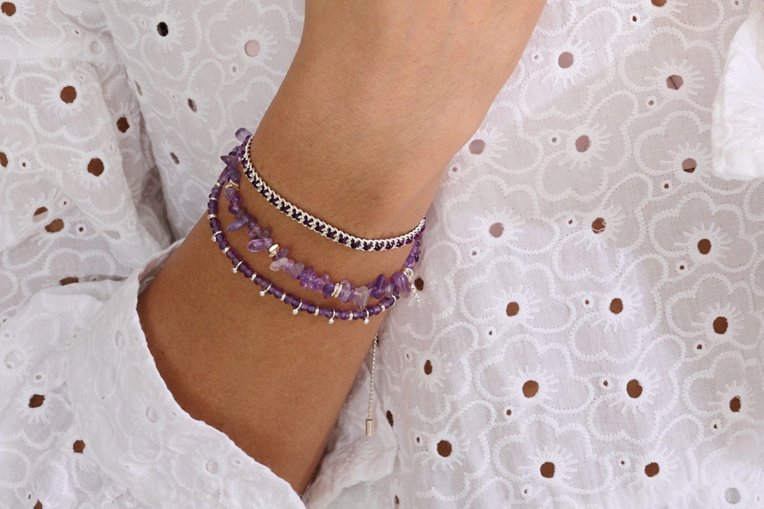 Stack of Amethyst gemstone silver bracelets on a wrist a white broidery angles dress . featuring the Harmony Amethyst gemstone bracelet, sana Amethyst crystal bead bracelet and the lilia woven braided bracelet. The perfect christmas gift for her.