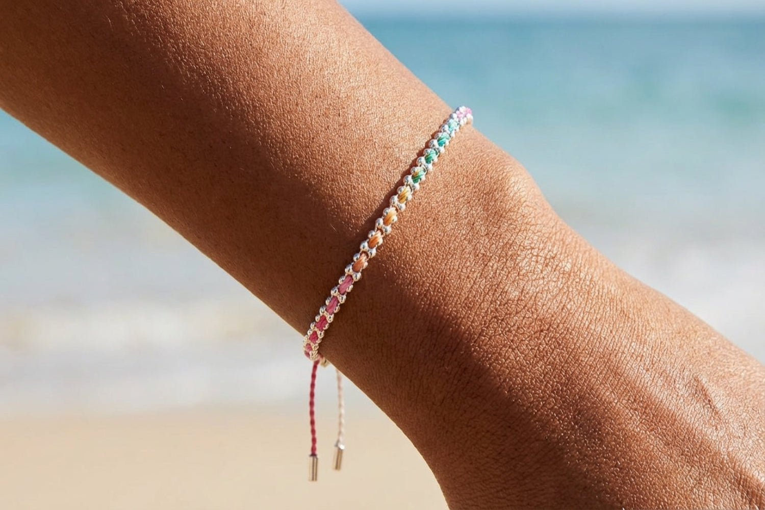 Silver woven bracelet with colorful threads resting on white marble surface with grey veining, showcasing craftsmanship and vibrant hues.