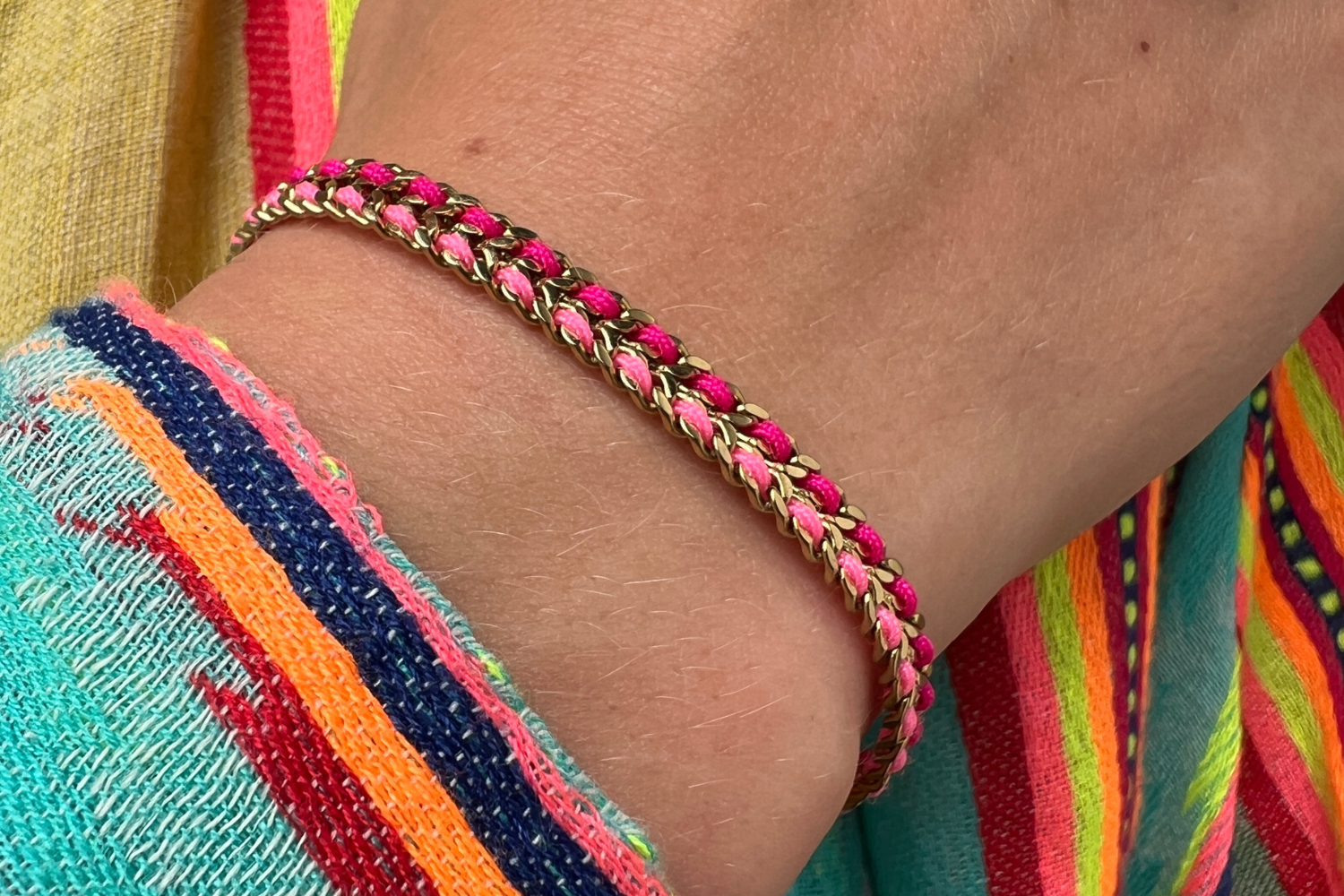 Cari magenta and pink woven bracelet styled on the wrist, a bright and playful gold friendship bracelet perfect for stacking and summer styling.