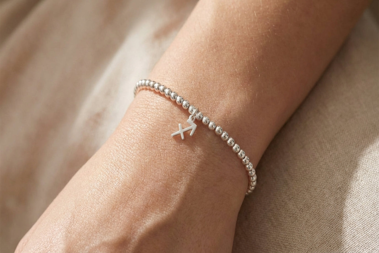 Detailed close-up of a female wrist wearing a silver Sagittarius zodiac bead bracelet, highlighting the slender chain and intricate charm against soft blurred background.