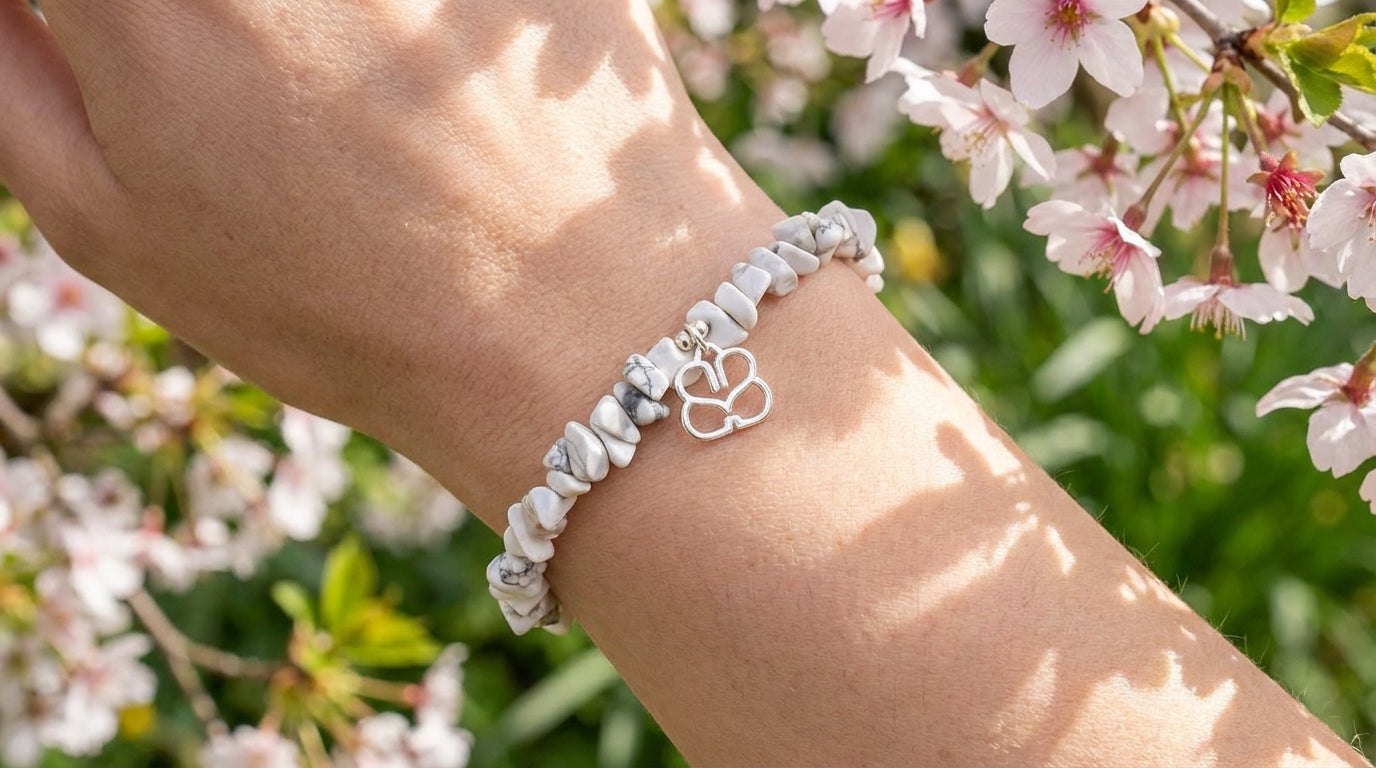 Close-up of a silver beaded white Howlite crystal bracelet on a female wrist in a spring outdoor setting with flowers and soft sunlight, highlighting intricate chain and charm details.