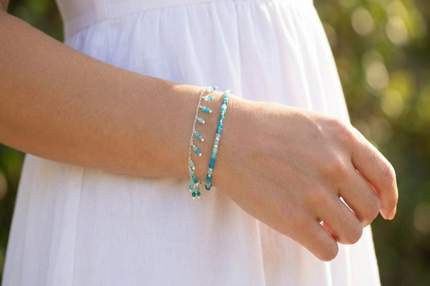 Close-up of a woman with light skin wearing a white summer dress showcasing the Amazonite and Apatite silver bracelet on her wrist, highlighting its fine texture and gemstones.