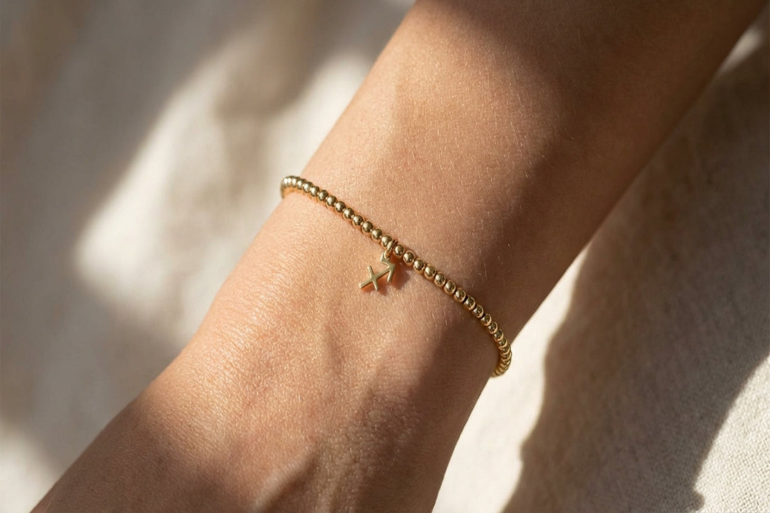 Close-up of a female model's wrist wearing a small gold Sagittarius zodiac charm bracelet, highlighting the fine chain and detailed charm in natural light.