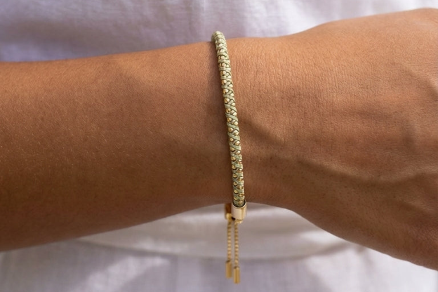 handwoven emelia pale green gold bracelet on models wrist with a white dress