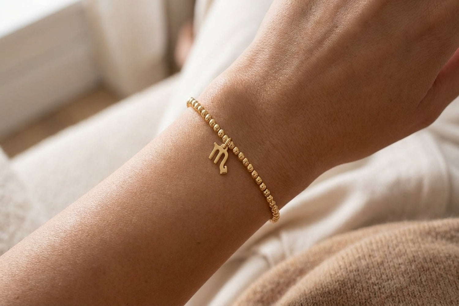Female model wears a delicate gold Scorpio zodiac bracelet in a cozy setting, highlighting its fine craftsmanship and subtle luxury.