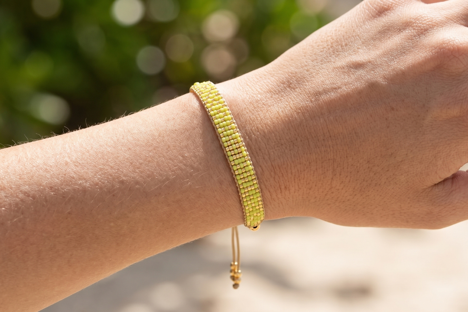Close-up of a vibrant gold and lime beaded friendship bracelet on a female model's wrist, highlighting bead details and colors in natural light.