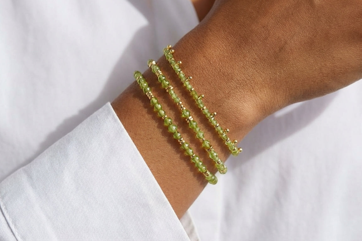 Moala Gold & Peridot Beaded Stacking Bracelet on a models arm showing green details with gold accents with a white shirt background.