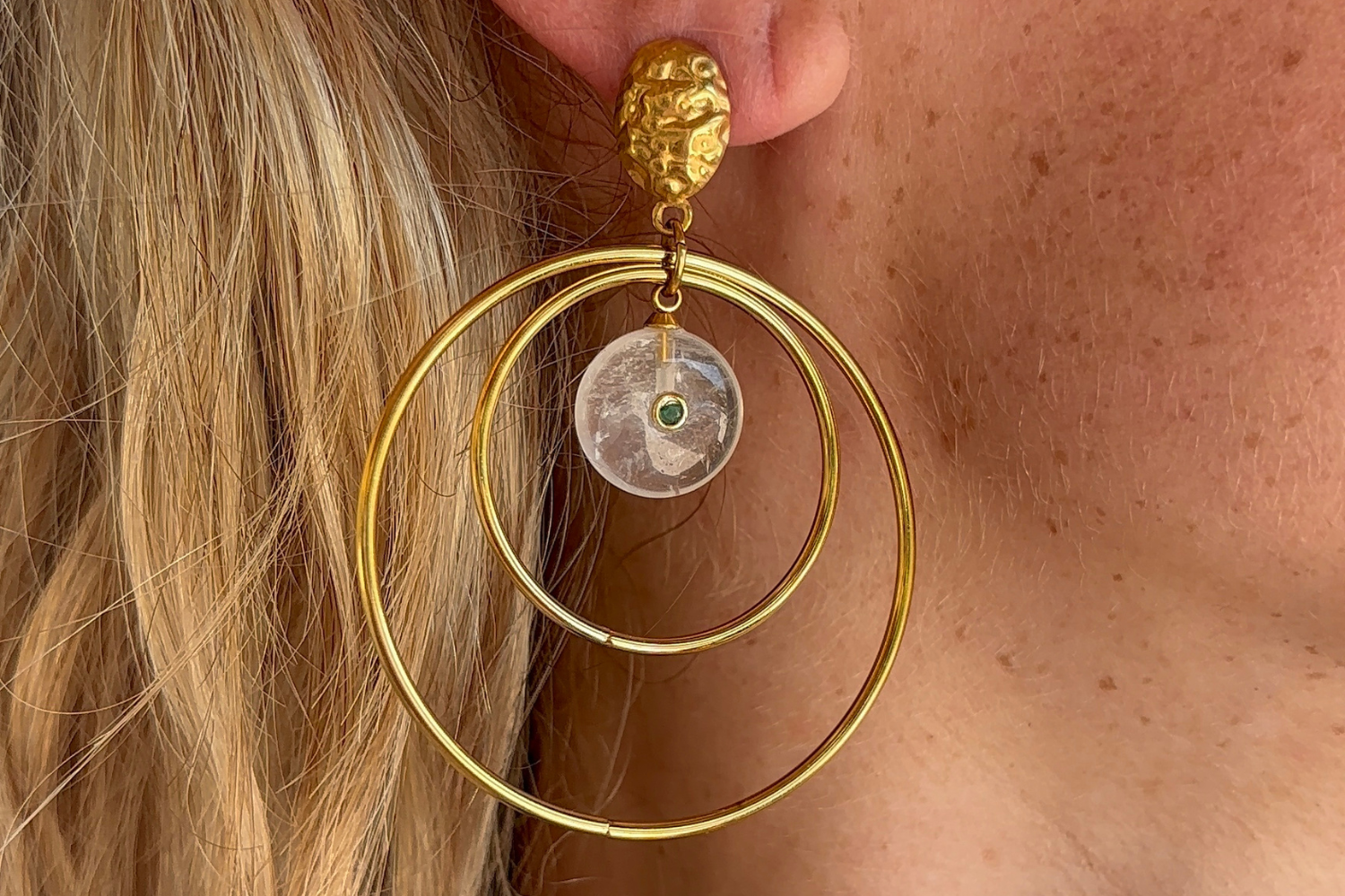 Model wearing Onda White Jade Gold Statement Earrings featuring white jade gemstone drops, green crystal accents and waterproof 14k Gold PVD double hoop design.