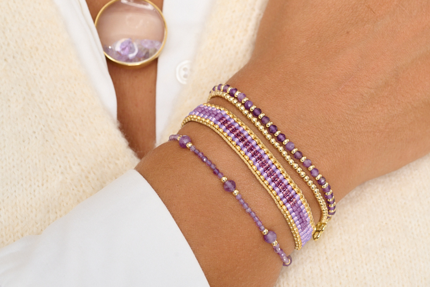 Palmeira Amethyst and Gold Bracelet Stack styled on the wrist, showcasing layered amethyst gemstone beads, purple woven textures and warm gold details.