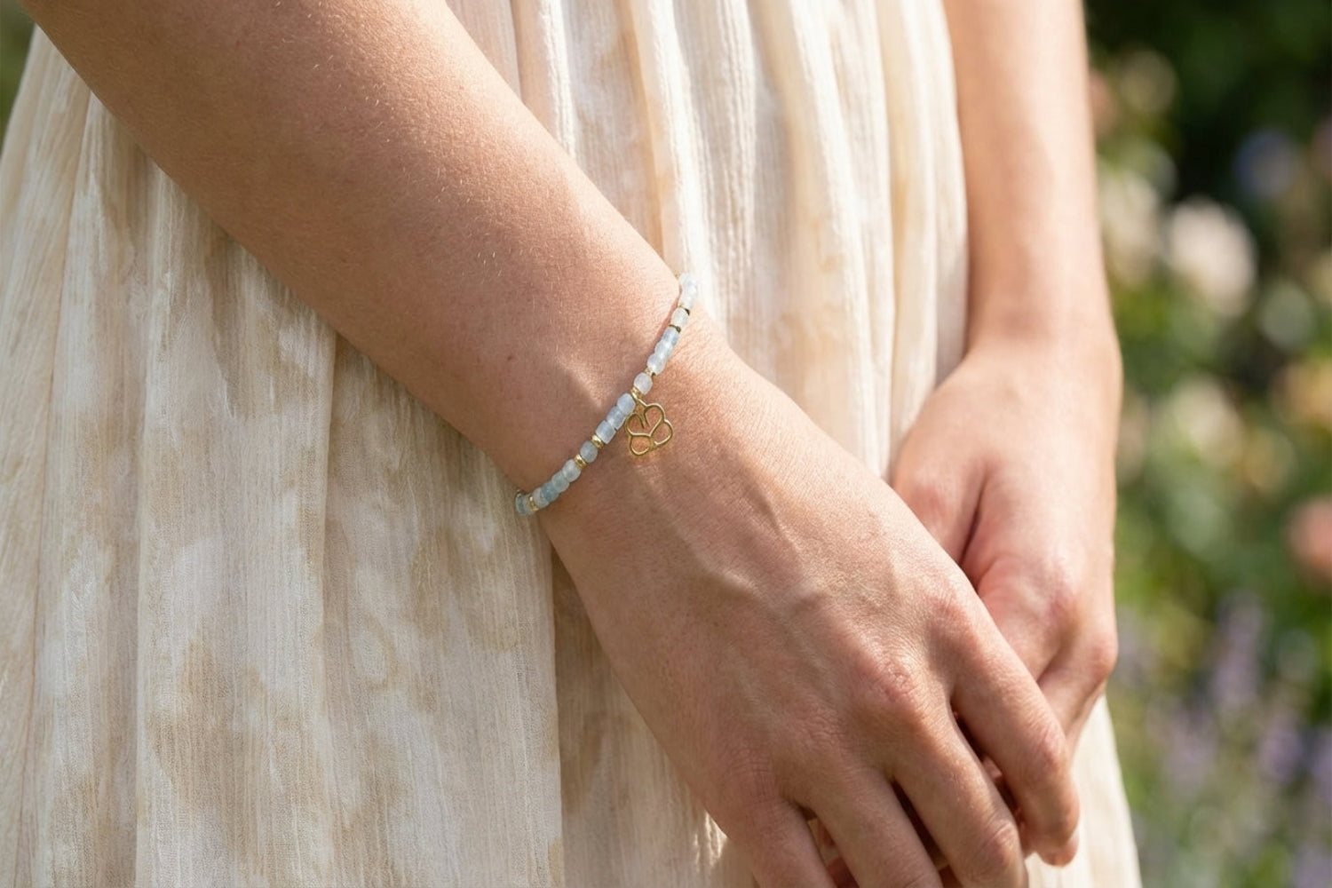Close-up of a delicate aquamarine gemstone bracelet with gold accents on a model's wrist in front of a dress, highlighting bead details and shimmer.