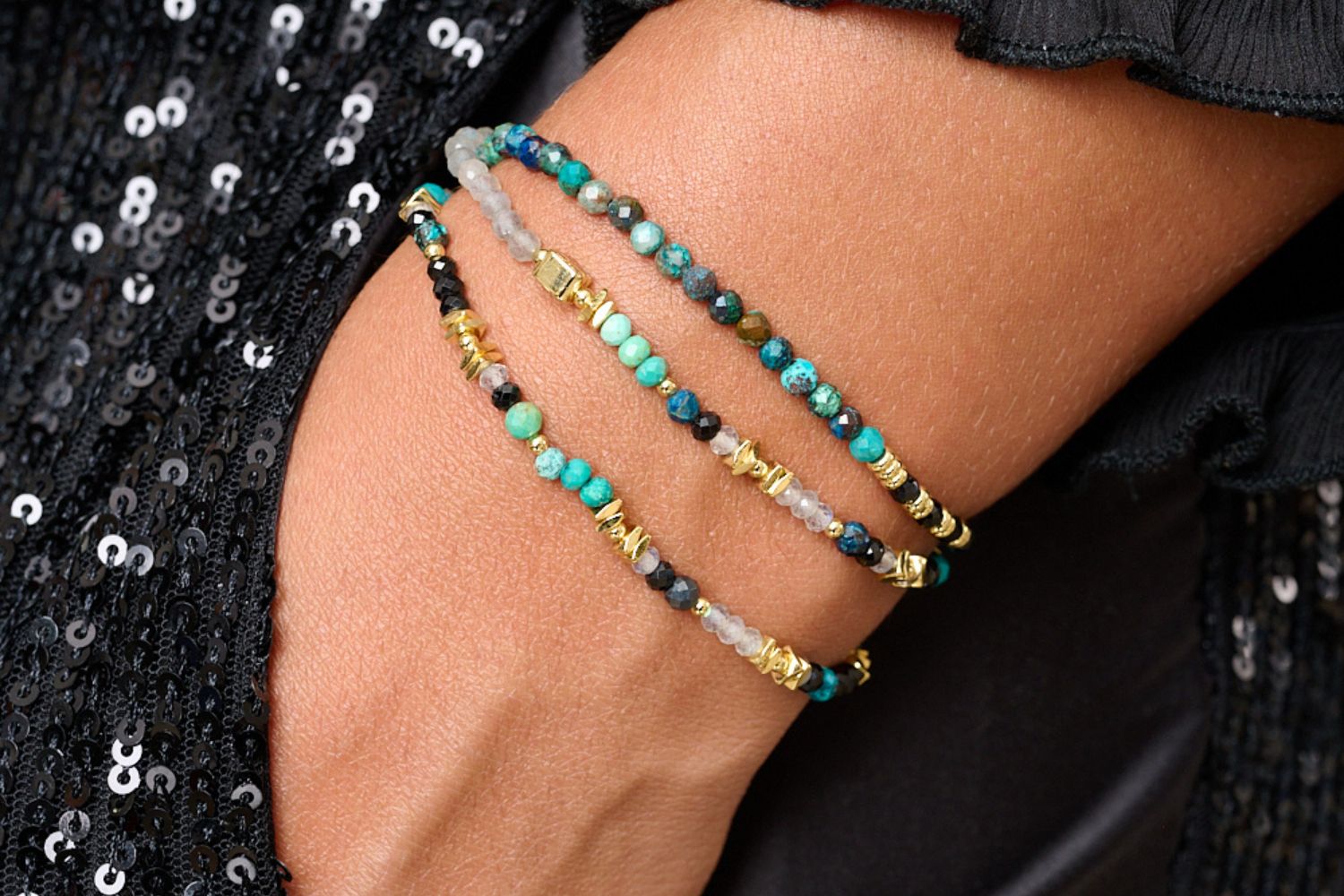 Close-up of a person's wrist wearing the Amaryllis triple-wrap stretch bracelet elegantly worn  with an elegant black silk shirt and black sequined trousersThe perfect gift  Christmas gift for her