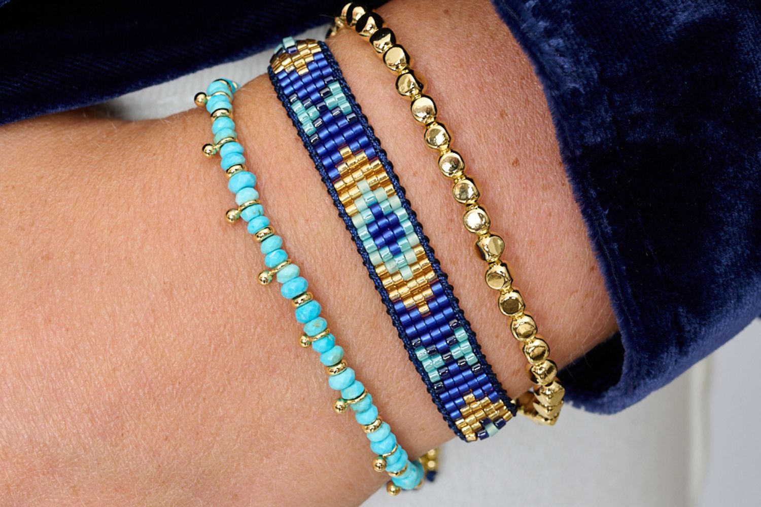 Close-up of a wrist wearing two beaded bracelets with blue, gold, and turquoise beads.