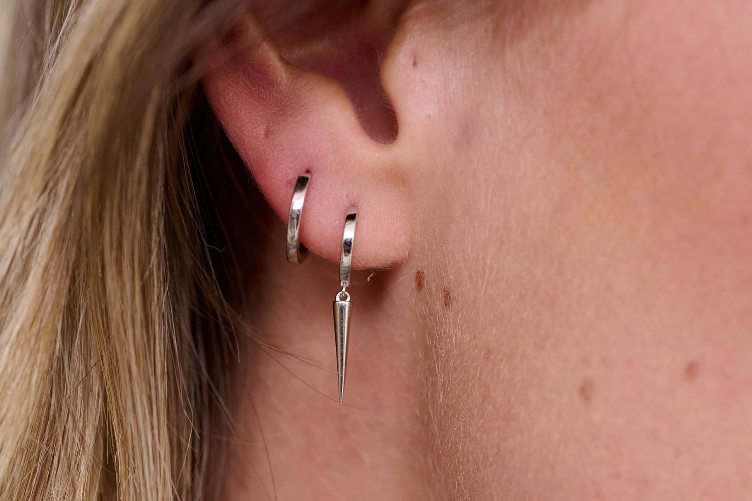 Model showcasing a lifestyle picture layering earrings. The first piercing shows the wonderful Caplan Sterling Silver spear huggie, layered with the reddy sterling silver huge in the second piercing.