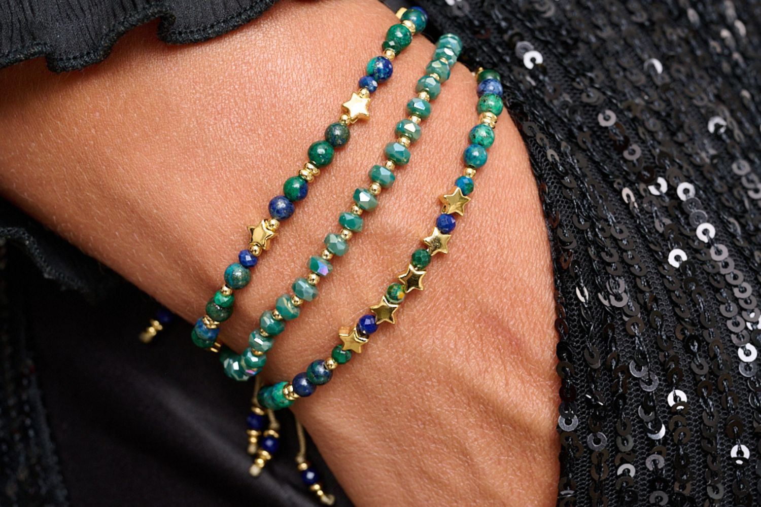 Close-up of a  multiple green beaded bracelets on a black sequin fabric background. Green prunus crystal stretch bracelet nested in between 2 star gemstone azurite bracelets. The perfect Christmas gift for her