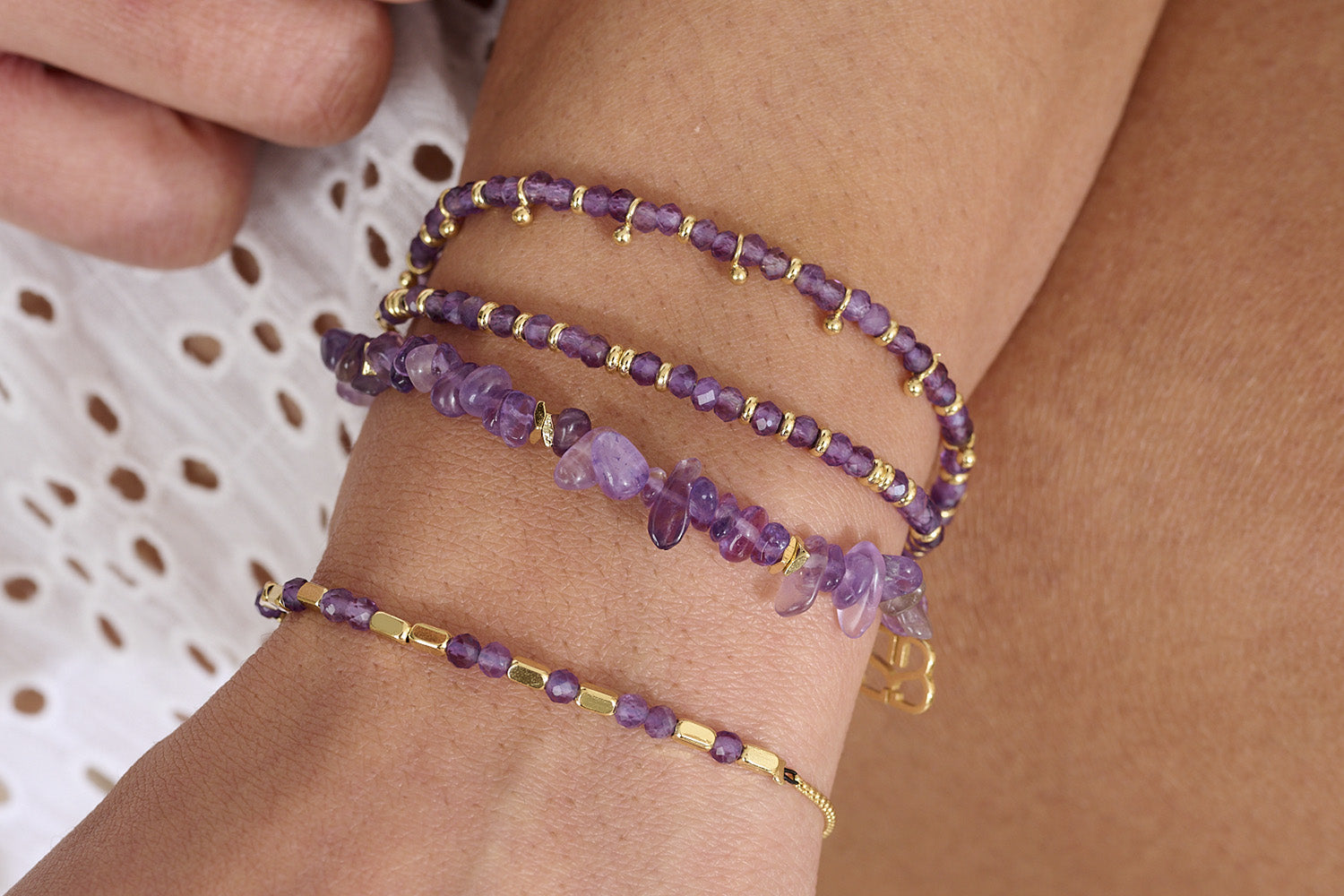 Close-up of a wrist wearing four purple  Amethyst gemstone beaded bracelets with gold accents. Stylish layering bracelets and the perfect day to night jewellery and Christmas gift for her.