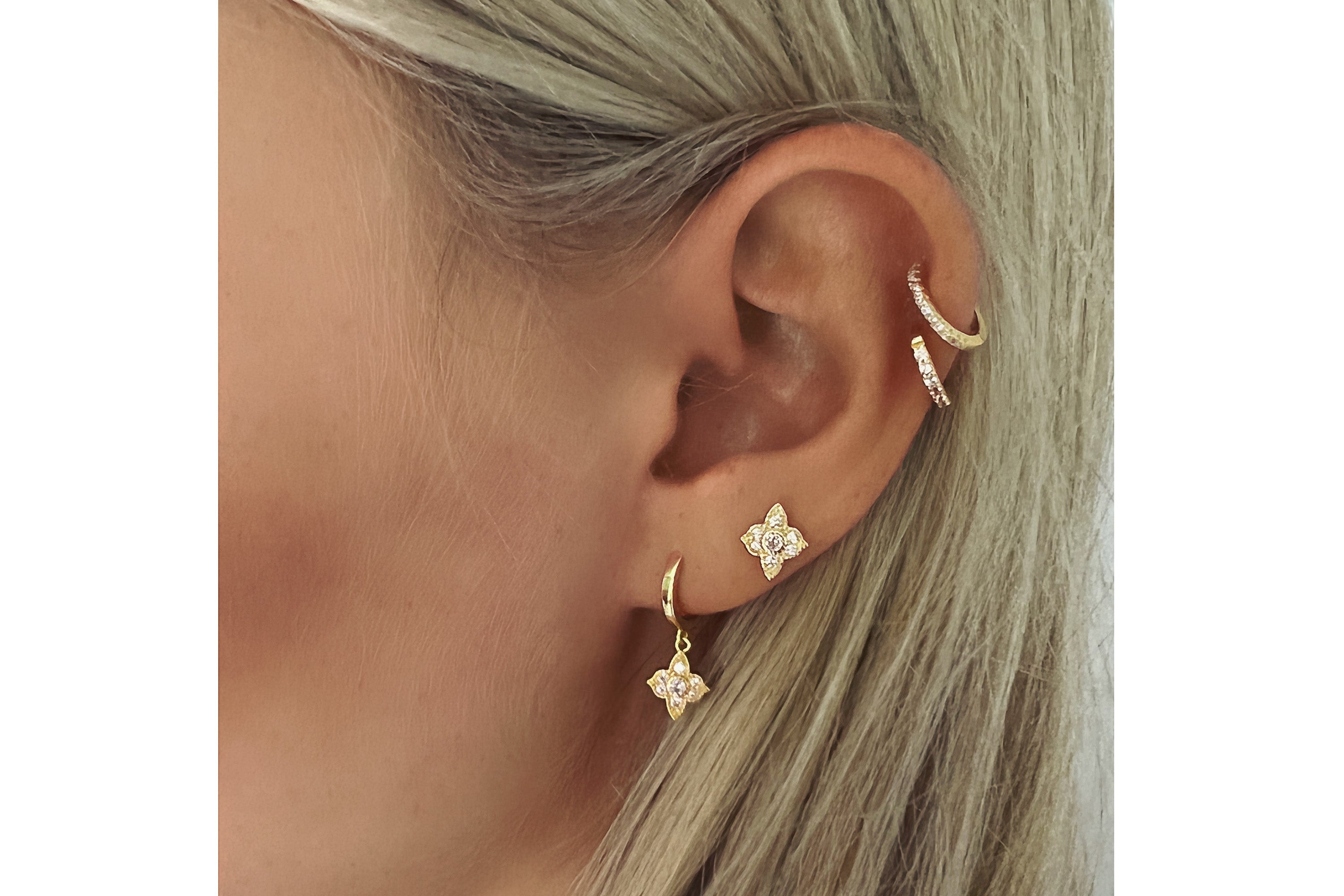 Close-up of an ear wearing gold hoop earrings with star-shaped charms on a white background