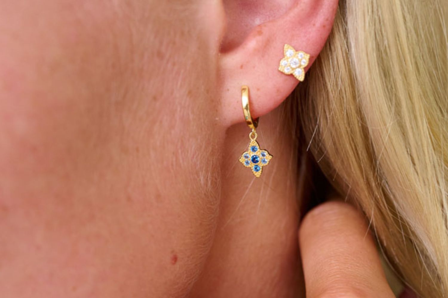 Close-up of a person wearing gold fop huggie sterling silver earring layered alongside a clear CZ sterling silver stud earring