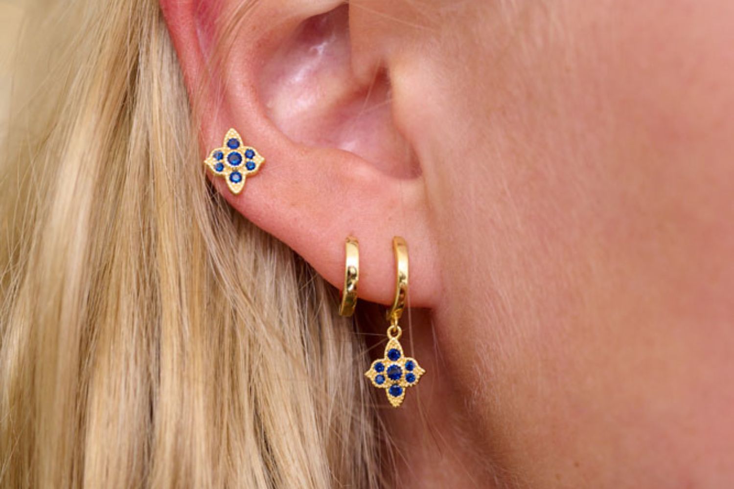 Close-up of a person wearing Boho Betty gold sterling silver Hoop Huggie earrings with blue CZ stones. Perfect earring layering 