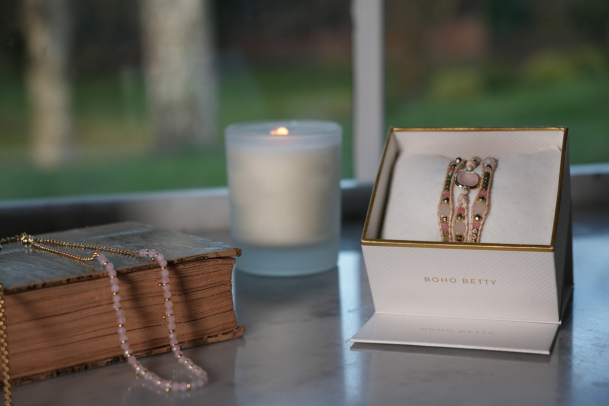America rose quartz wrap bracelet gift boxed by a candlelit window with a rose quartz necklace draped over a vintage book