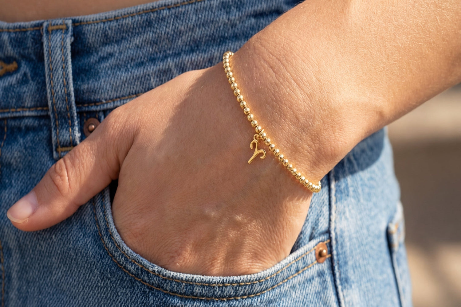 High-resolution shot of gold Aries zodiac charm bead bracelet resting on polished marble surface, emphasizing fine beads and detailed charm.