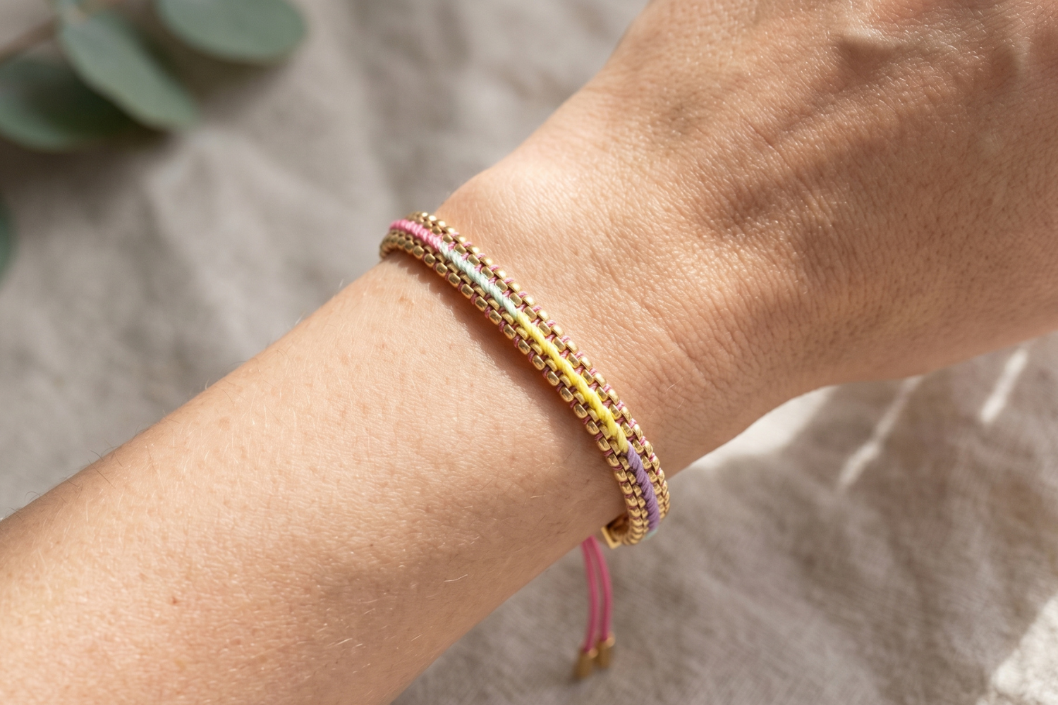 Bloom pastel rainbow woven bracelet styled on the wrist, a soft colourful gold friendship bracelet perfect for stacking and summer styling.