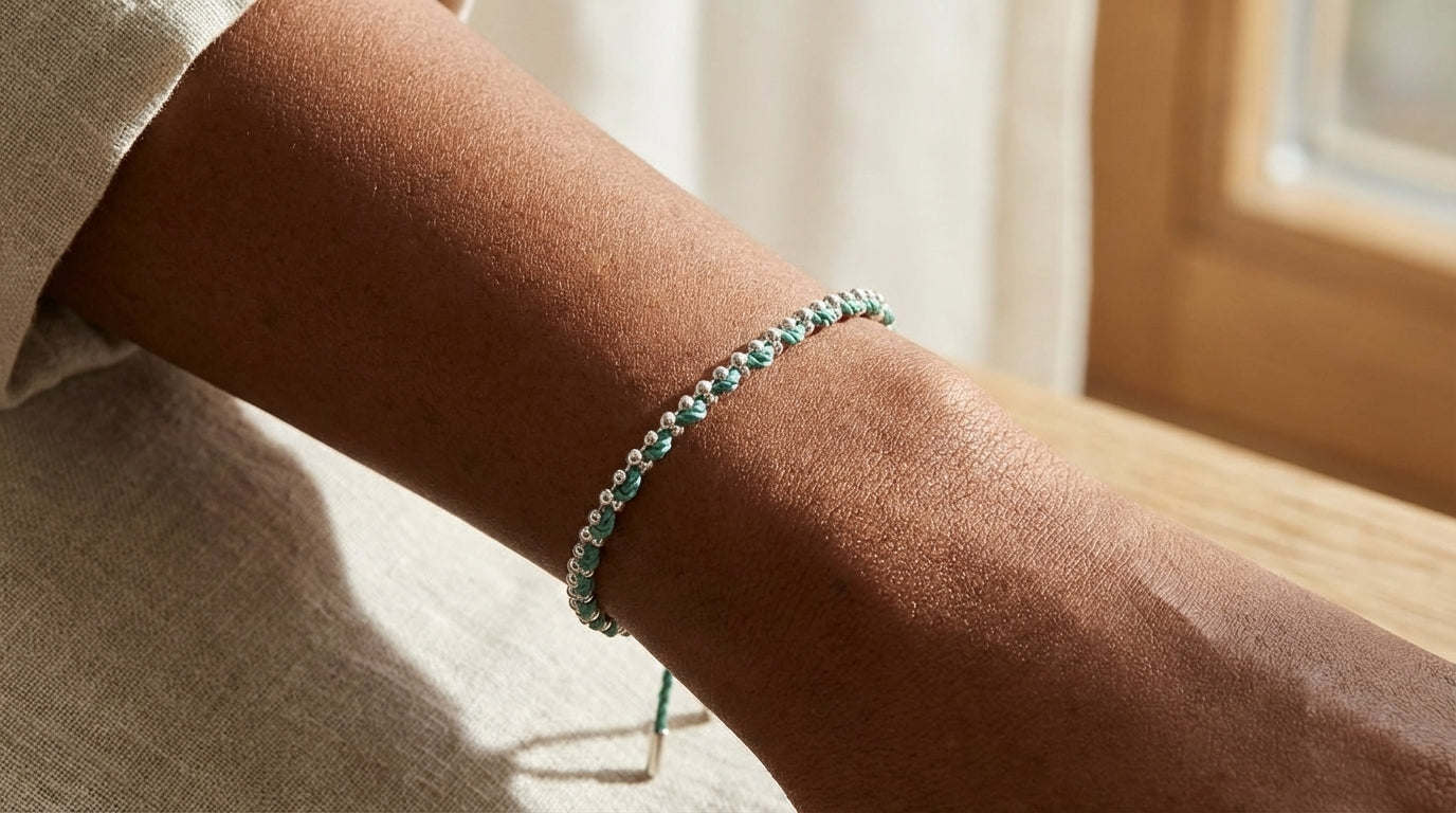 Close-up of teal and silver braided friendship bracelet on a female model's wrist, highlighting craftsmanship and metallic beads.
