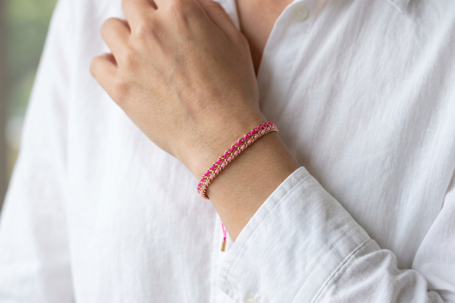 Cari magenta and pink woven bracelet styled on the wrist, a bright and playful gold friendship bracelet perfect for stacking and summer styling.
