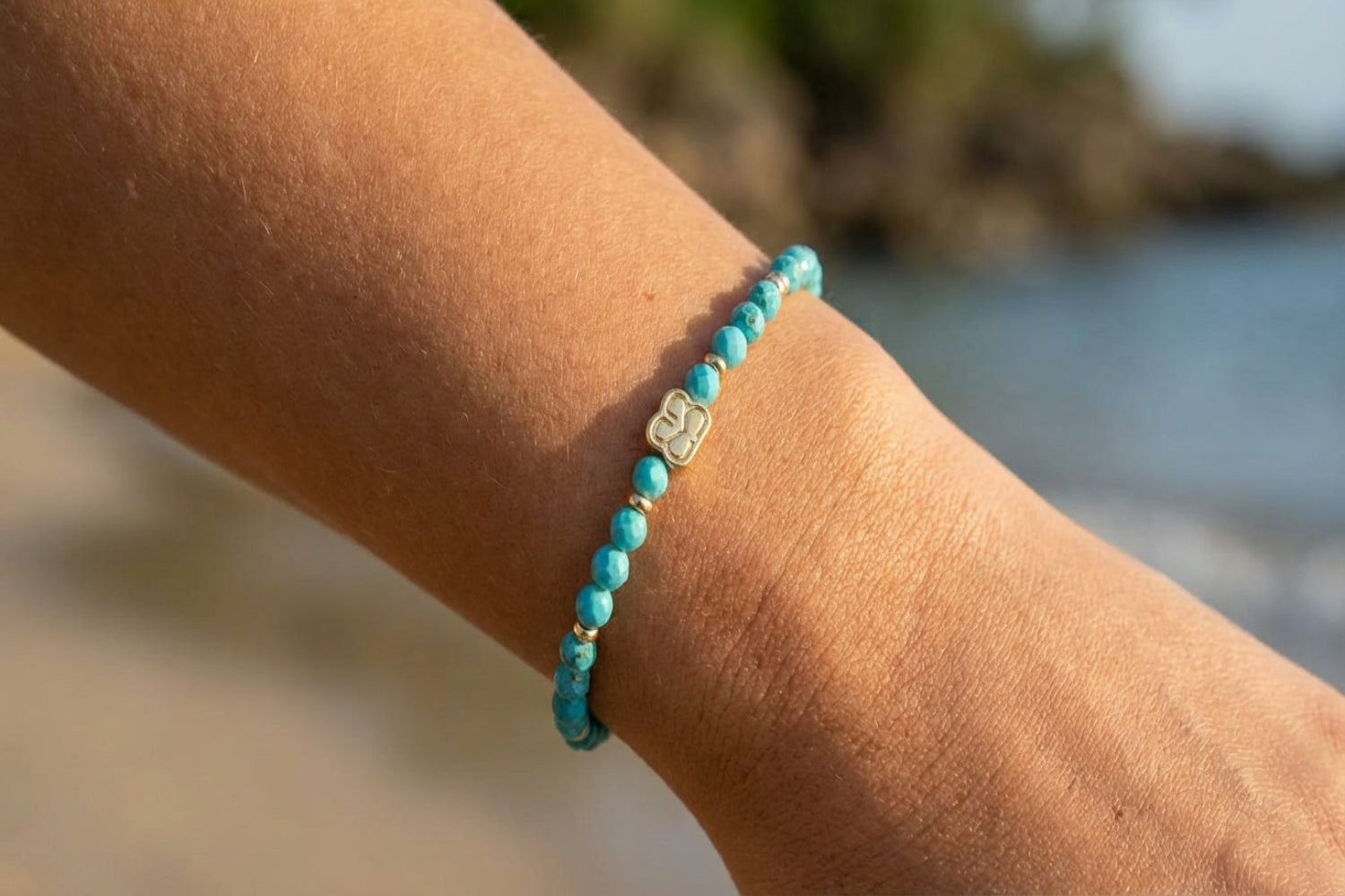 Close-up of a delicate gold chain bracelet with turquoise Howlite beads and charms, highlighting faceted details on a slightly tanned wrist in natural light.