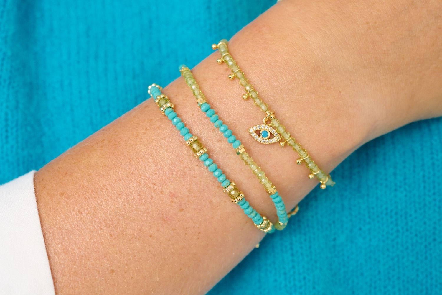 A lifestyle shot showcasing perfect bracelet layering of the delight peridot and turquoise bracelet in a look with other mixed bracelets in effortless styling with a turquoise jumper.