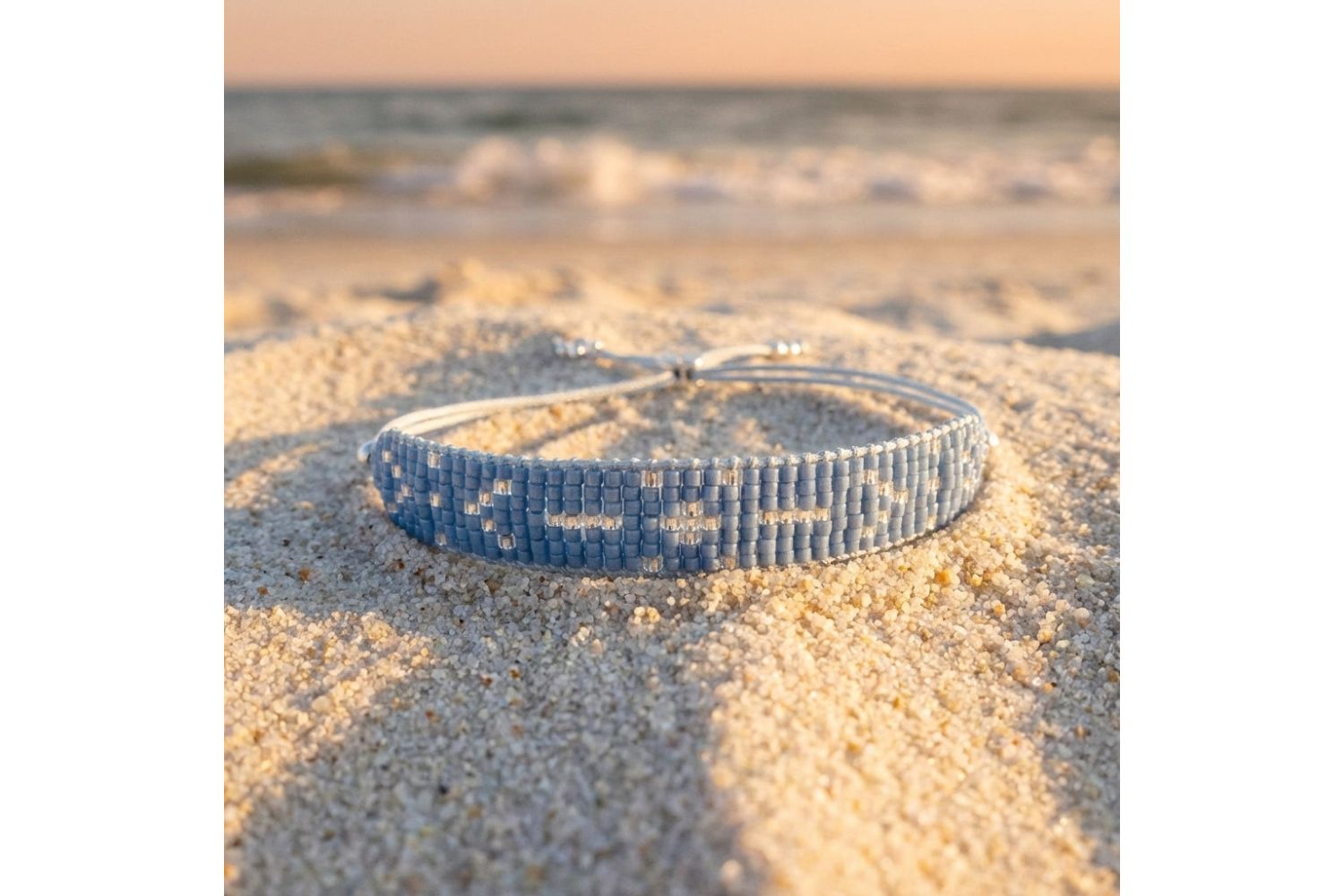 Grace silver and blue beaded friendship bracelet resting on soft sand during golden hour, emphasizing casual summer boho-chic style.