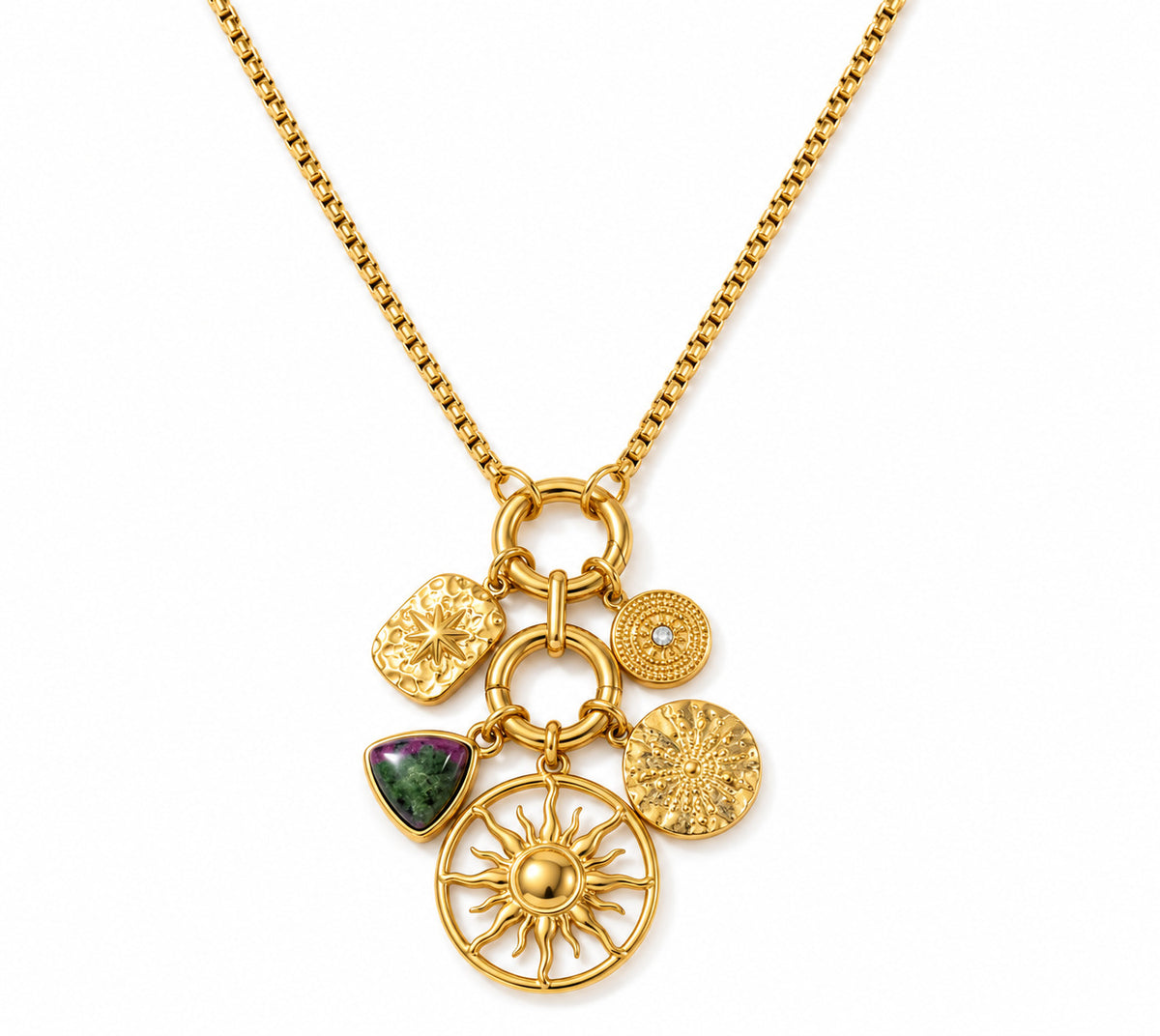A gold chain necklace with a multi-charm pendant featuring a large sunburst, textured circular charms, a small round charm with a clear stone, and a green and pink gemstone charm, shown on a white background.