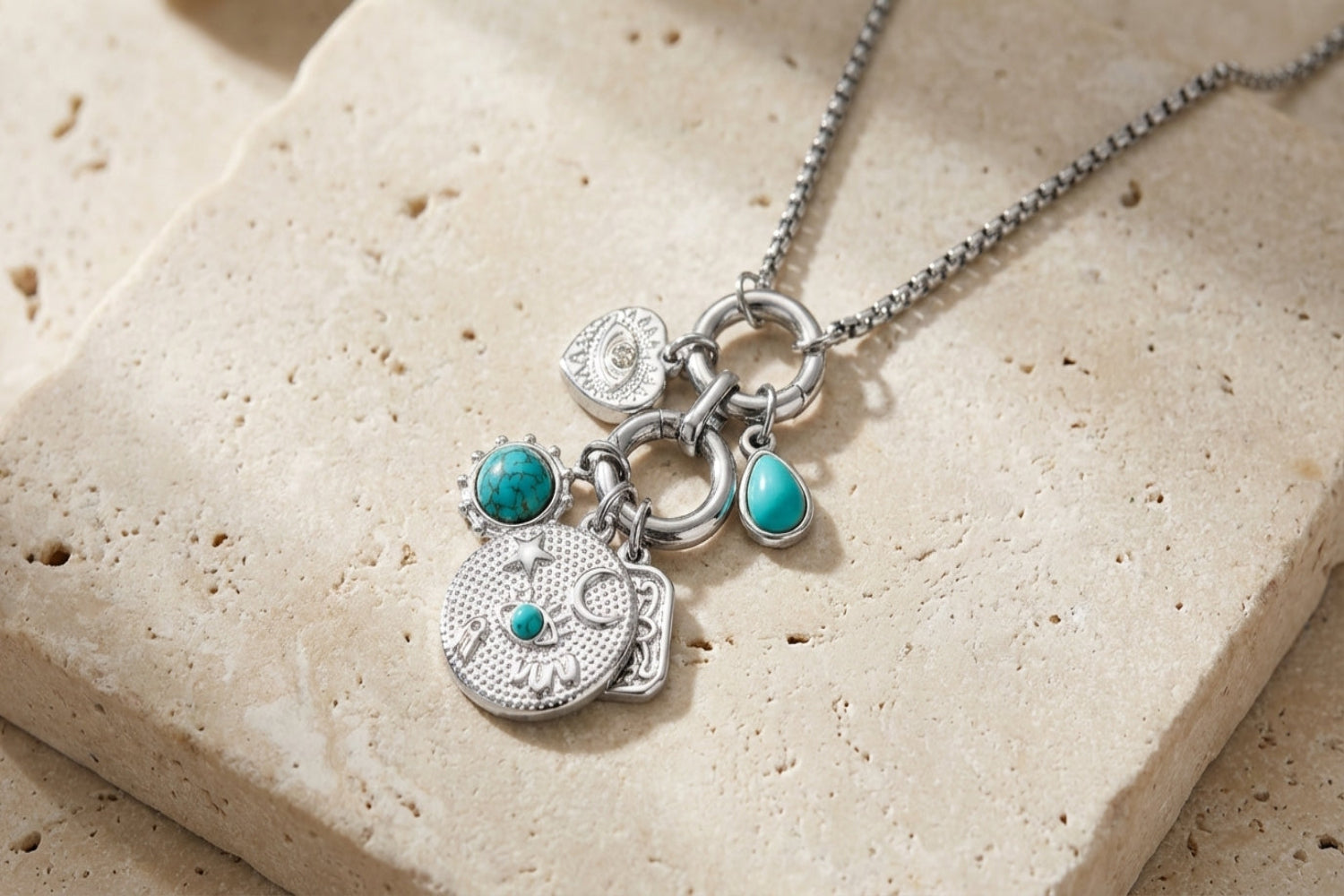 Close-up of Hemani turquoise howlite charm necklace on textured neutral surface highlighting steel chain and vibrant turquoise charms