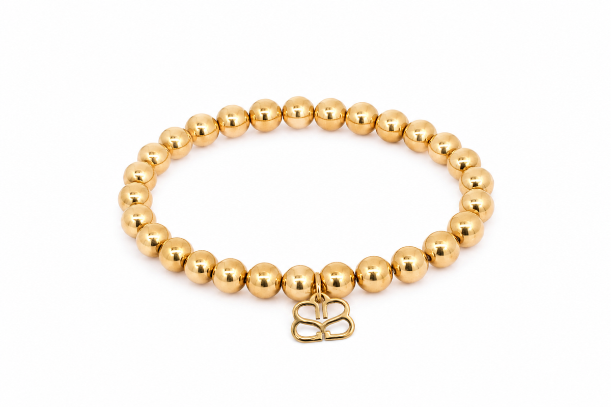 Lissette Gold Bead Stretch Bracelet featuring smooth polished gold-tone beads, Boho Betty’s signature gold BB filigree charm and waterproof 14k Gold PVD-coated stainless steel.