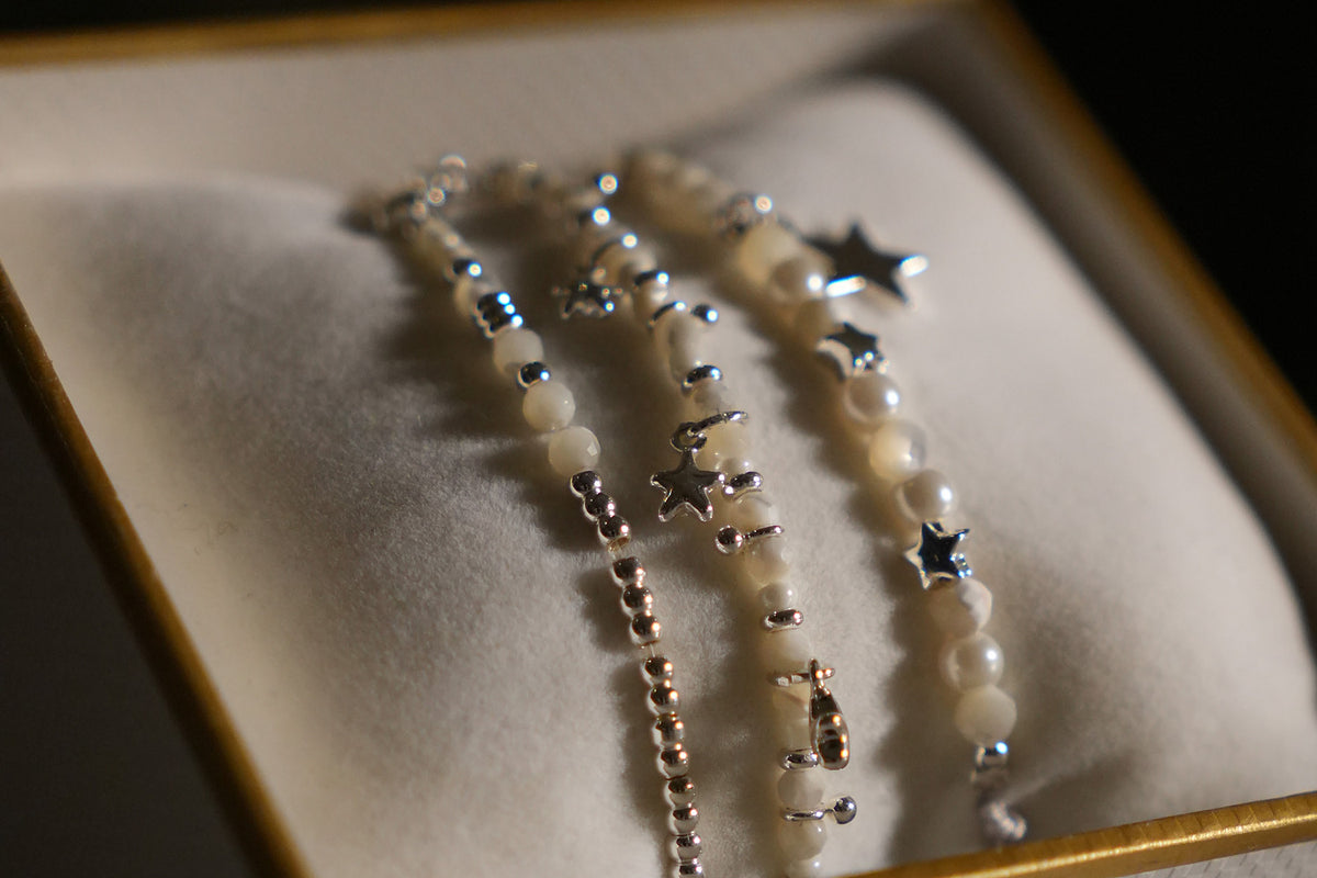 Close-up of the Orion White Pearl & Silver Star Bracelet Stack showing mother of pearl beads, silver balls and silver star charms on a white cushion