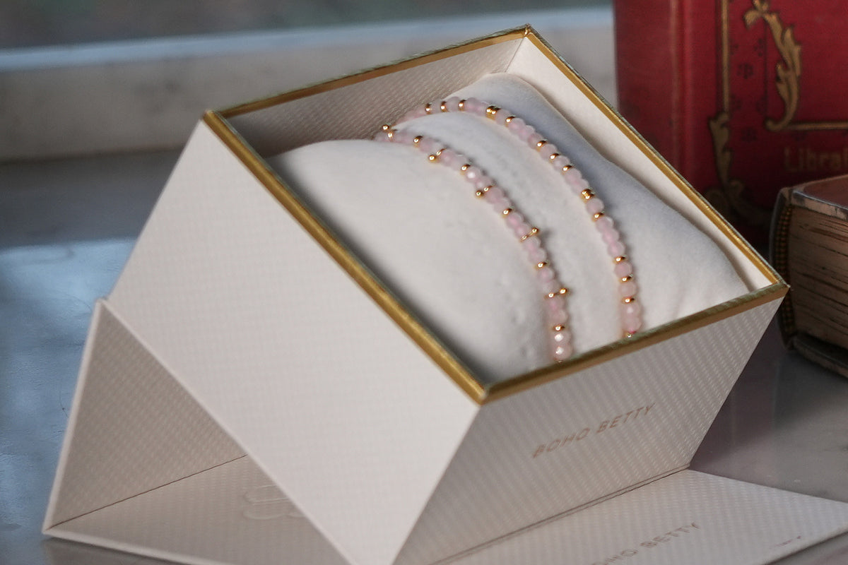 Serenity Rose Quartz Bracelet Stack of pink rose quartz and gold bead bracelets in an open Boho Betty gift box