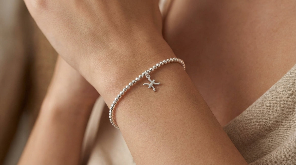 Close-up of a silver Pisces zodiac charm bracelet on a female wrist, showing detailed micro-texture, stretch beads, and delicate charm.