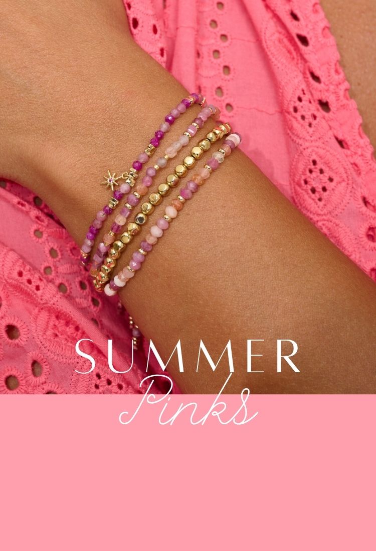A close-up of a woman’s wrist adorned with layered Boho Betty gemstone bracelets in shades of pink, magenta and gold, featuring delicate beads and a tiny star charm. She wears a vibrant pink eyelet dress, evoking a joyful, sun-drenched summer vibe.
