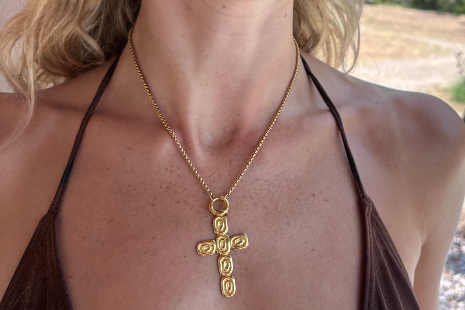 Thalia Short Gold Cross Necklace worn layered on the neckline, showcasing a contemporary sculptural gold cross pendant on a waterproof 14k gold PVD chain.