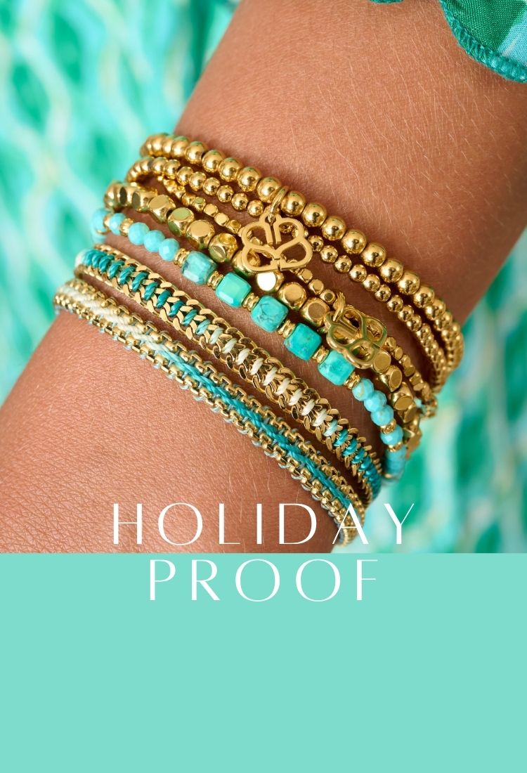 A smiling woman wears bold gold Boho Betty jewellery, including a chunky chain necklace, matching bracelet, and statement earrings. Her green and white patterned dress complements a close-up of stacked waterproof bracelets in turquoise and gold, showcasing intricate textures and durable design. The text “Holiday Proof” appears in the centre.