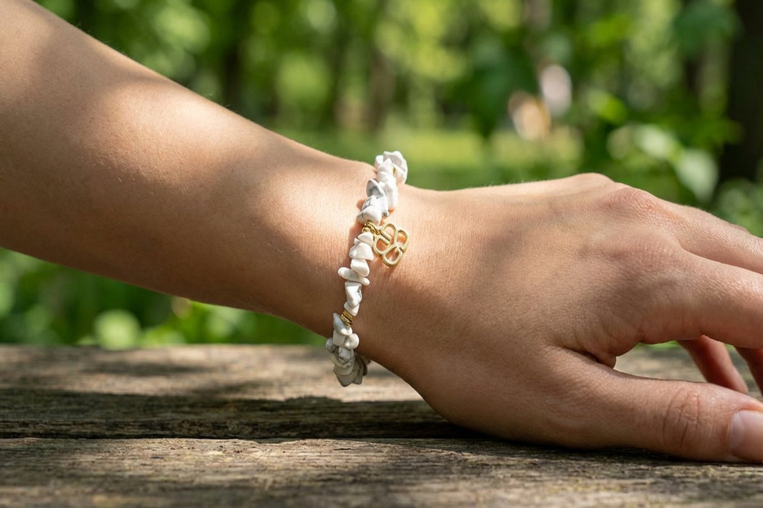 White Howlite crystal bead bracelet with gold accents on female model's wrist in outdoor park setting.