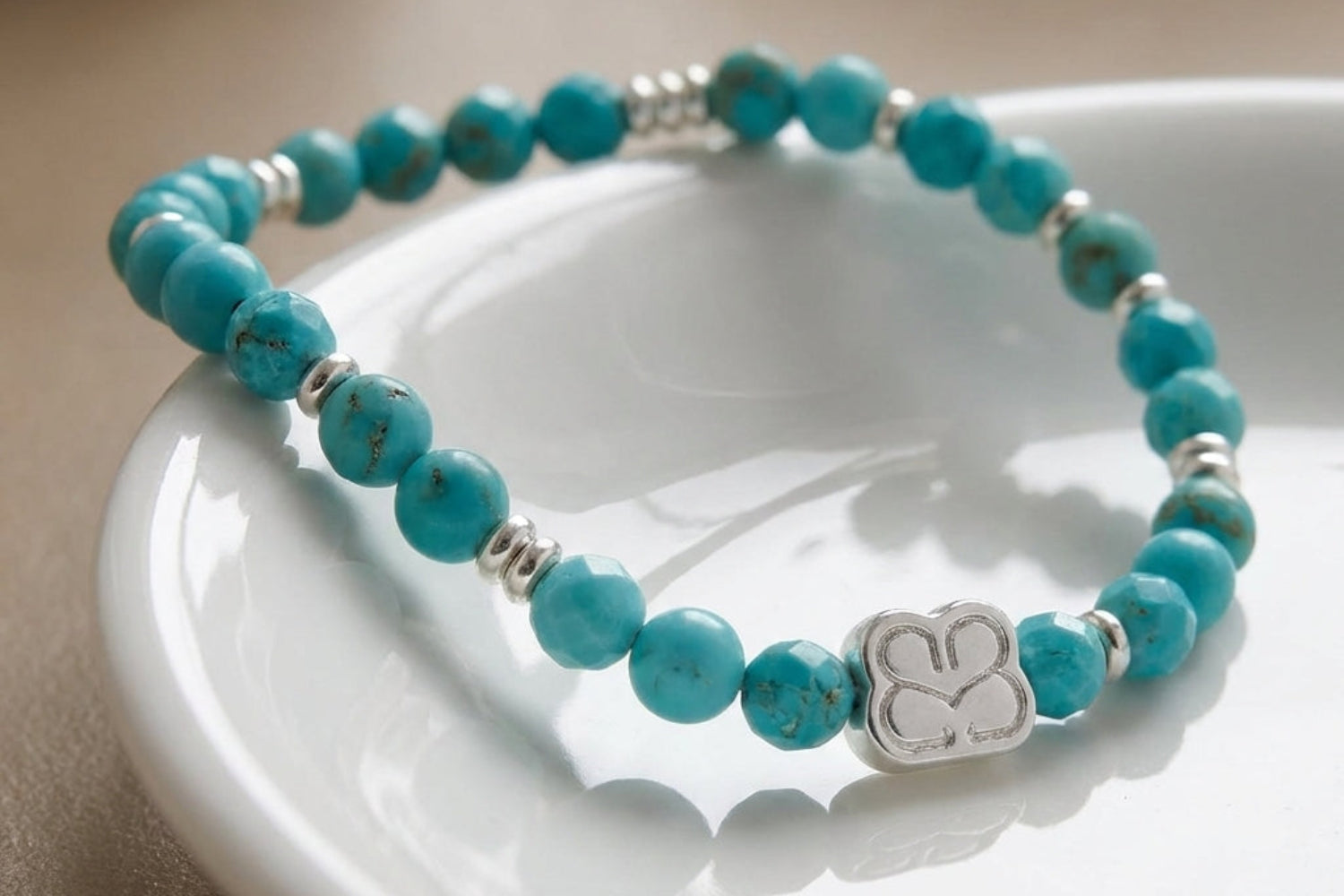 Close-up of the Wonder turquoise howlite beaded bracelet draped over white ceramic dish, capturing micro-textures, silver flashes, and tranquil hues.